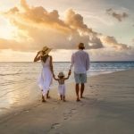 A elegant family in white summer clothing walks hand in hand down a tropical paradise beach during sunset tme and enjoys their vacation time