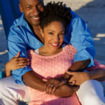 African American couple sitting and embracing on beach.