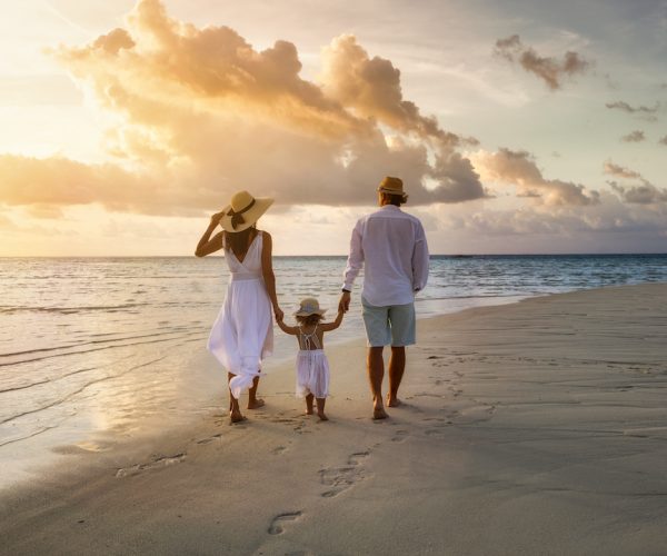 A elegant family in white summer clothing walks hand in hand down a tropical paradise beach during sunset tme and enjoys their vacation time