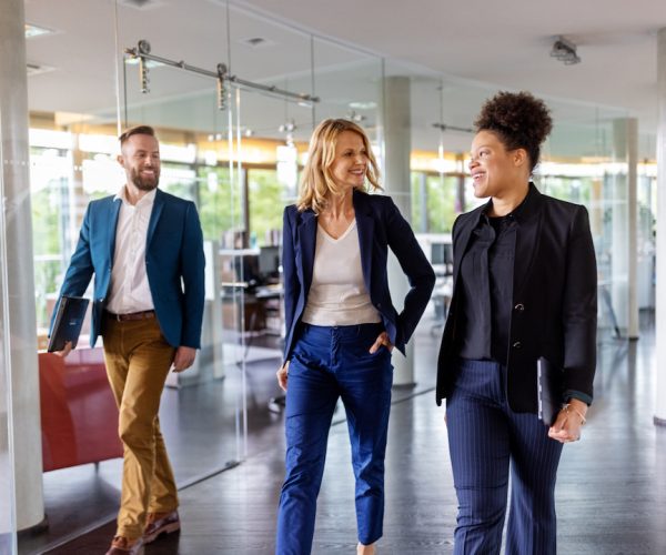 Group of multiracial businesspeople discussing while walking through the office. Team of corporate professionals moving through the office corridor.