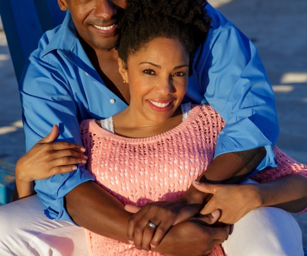 African American couple sitting and embracing on beach.